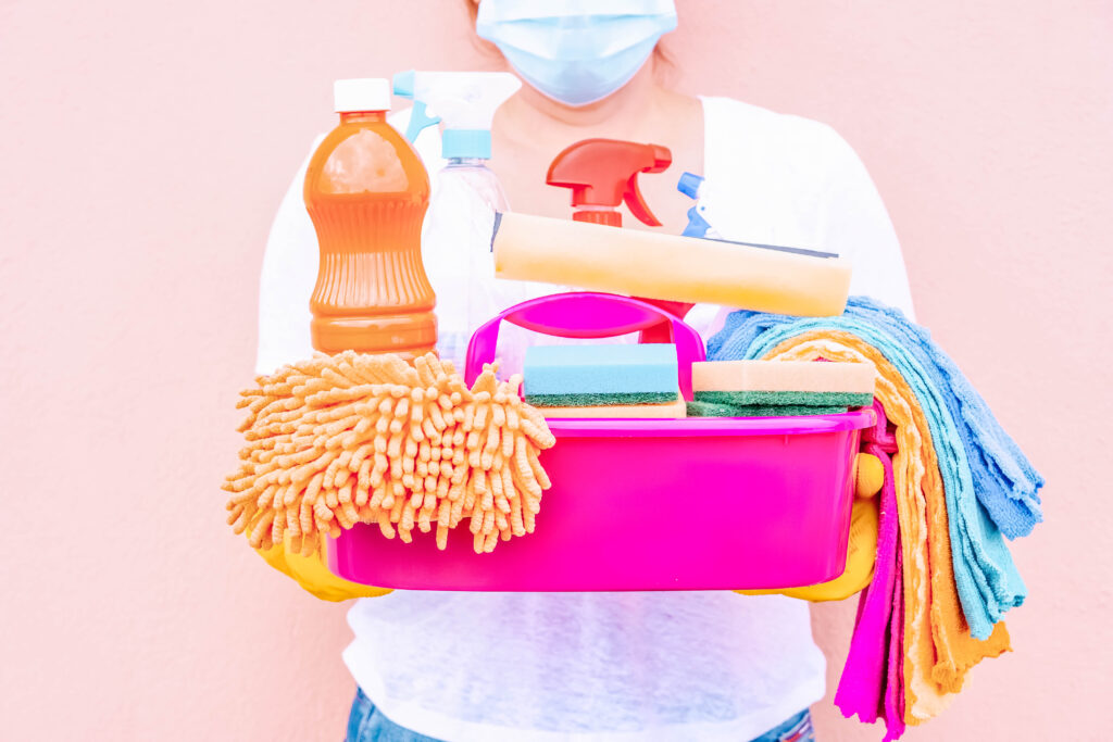 cleaning lady or housewife - caucasian woman in mask holding basin with cleaning supplies, spring clean concept