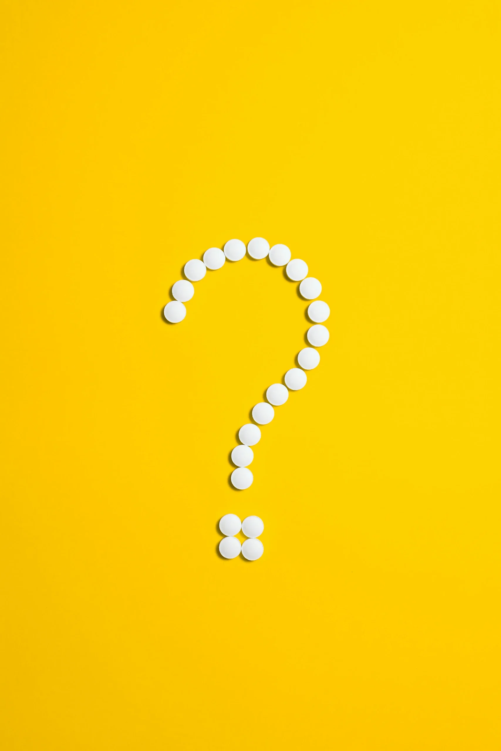 Tablets placed in the shape of a question mark on a yellow background